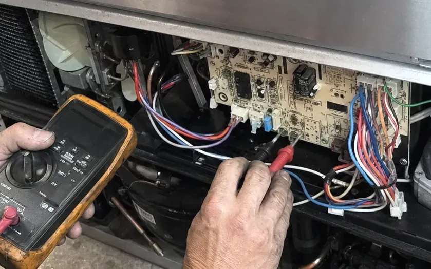 Technician testing a control board and its color-coded wiring with an orange multimeter.