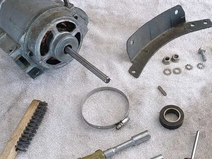 Fan motor, a hose clamp, a curved bracket, nuts and a wire brush laid out on a white towel.